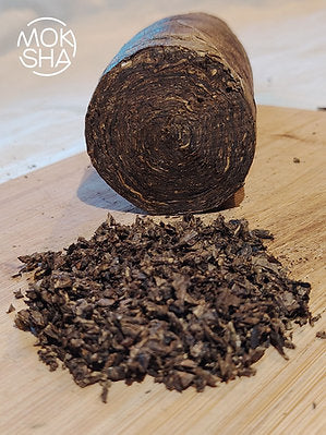 Rolled mapacho leaf with scattered pieces on a wooden surface, branded 'Moksha'.